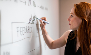 Red headed woman writing feedback on whiteboard